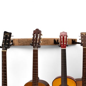 May include: A wooden guitar rack displaying four acoustic guitars. The guitars have varying body and headstock colours. The rack is made from a weathered wooden beam with black metal guitar holders.