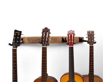 May include: A wooden guitar rack holding four acoustic guitars. The guitars have different colored bodies and headstocks. The rack is made of a weathered wooden beam with black metal guitar holders.