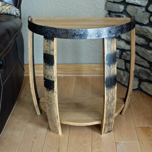 May include: A half-circle side table made from reclaimed wood and metal. The tabletop is light brown, supported by curved wooden legs with black accents. A metal band wraps around the top. The table has a lower shelf for storage.