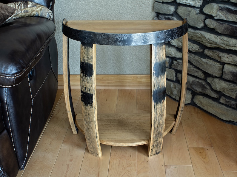 May include: A half-circle side table made from reclaimed wood and metal. The tabletop is light brown, supported by curved wooden legs with black accents. A metal band wraps around the top. The table has a lower shelf for storage.