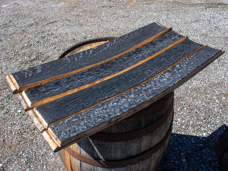 May include: A set of three curved wooden barrel staves featuring a deeply charred, textured black finish on the outer surface and a natural light brown wood tone on the edges, arranged horizontally to form a flat, rectangular surface.