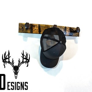 May include: A wooden hat rack with three metal hooks. The rack is made from reclaimed wood and has a rustic finish. A black baseball cap is hanging on one of the hooks.