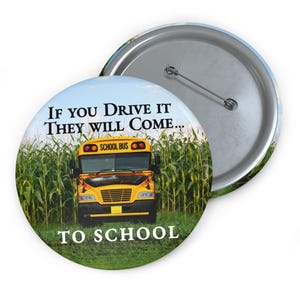 Puede incluir: Un botón redondo con un gráfico de autobús escolar amarillo frente a un campo de maíz. El texto en el botón dice "IF YOU DRIVE IT THEY WILL COME... TO SCHOOL". El botón tiene un alfiler de metal en la parte posterior.