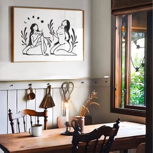 May include: A black and white line art print of two figures in a forest setting. The figures are facing each other and appear to be holding hands. The print is framed and hanging on a white wall.