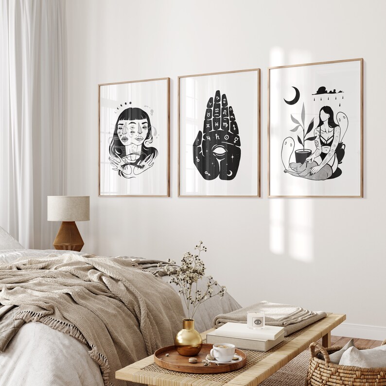 May include: Three black and white illustrations in frames on a white wall. The illustrations are of a woman with two faces, a hand with an eye and symbols, and a woman with a plant and a ghost.