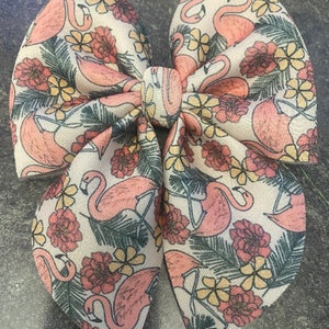 Könnte beinhalten: Eine weiße Schleife aus Stoff mit einem rosa Flamingo- und Blumenmuster. Die Schleife ist zu einem Knoten gebunden und hat eine Schlaufe oben.