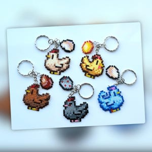 May include: A selection of pixelated chicken keyrings in various colours, including brown, yellow, and blue. Each keyring features a chicken design with a red comb and a small egg. The keyrings are attached to silver key rings.
