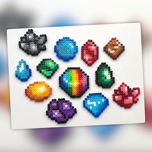 Op de afbeelding: Een verzameling van 12 kleurrijke pixel art edelstenen, waaronder een regenboog edelsteen, een paarse edelsteen, een blauwe edelsteen, een rode edelsteen, een groene edelsteen, een gele edelsteen, een zwarte edelsteen en een bruine edelsteen.