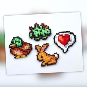Op de afbeelding: Vier kleurrijke pixel art-ontwerpen gemaakt met kralen. De ontwerpen omvatten een ​​groen monster, een bruine eend, een bruin konijn en een rood hart in een witte spraakballon.
