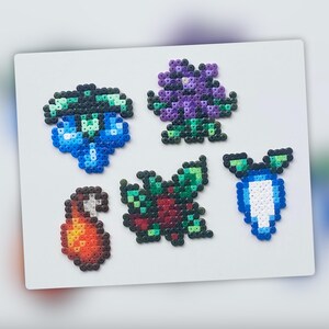 Op de afbeelding: Vijf kleurrijke pixel art-ontwerpen gemaakt met kralen. De ontwerpen omvatten een blauwe en groene bloem, een paarse bloem, een rode en groene bloem, een blauwe en witte bloem en een rode en oranje vlam.