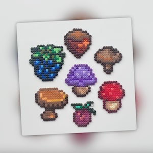 Op de afbeelding: Een set van zeven kleurrijke pixel art-ontwerpen van paddenstoelen en bessen. De ontwerpen zijn gemaakt met kleine plastic kralen en zijn gerangschikt op een witte achtergrond.