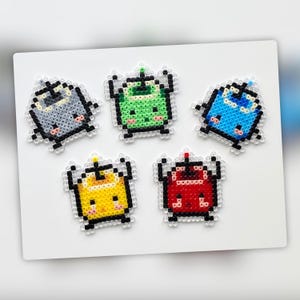 May include: Five colorful pixel art characters made with beads. The characters are a gray robot, a green alien, a blue robot, a yellow robot, and a red robot. Each character has a cute, cartoon-like face.