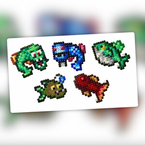 Op de afbeelding: Vijf pixel art-figuren gemaakt met kleurrijke kralen. De figuren zijn een groene vis, een blauwe vis, een groen-bruine vis, een bruine vis en een rode vis.