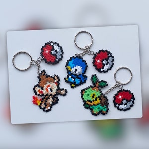 May include: Five colorful keychains featuring pixel art characters from the Pokemon video game series. The keychains are made of plastic beads and feature characters like Bulbasaur, Charmander, Squirtle, and Pikachu.