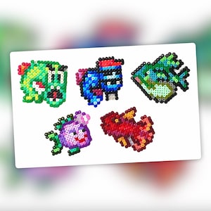 Op de afbeelding: Vijf kleurrijke pixelkunstfiguren gemaakt met kralen. De figuren zijn een groen en geel wezen met een brede mond, een blauw en rood wezen met een hoed, een groene en blauwe vis, een roze en paarse wezen met een bloem en een rood en roze wezen met vleugels.
