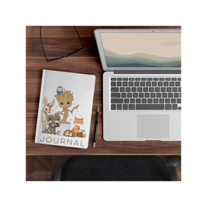 May include: A white journal with a colorful illustration of a cartoon Groot character from Guardians of the Galaxy surrounded by woodland creatures. The journal has the word "JOURNAL" printed in black at the bottom.