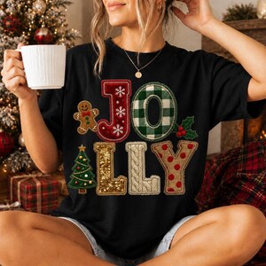 Puede incluir: Una camiseta negra con la palabra JOLLY en letras grandes y texturizadas. La J es roja con copos blancos, la O es de cuadros verdes y blancos, las L son de lentejuelas doradas y punto trenzado crema, y la Y es color canela con lunares rojos.