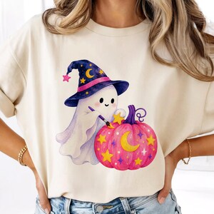 Puede incluir: Camiseta color crema con un dise&ntilde;o caprichoso de Halloween. Un fantasma amigable con un sombrero de bruja pinta una calabaza rosa con estrellas amarillas y una luna creciente. El fantasma sostiene un pincel, creando una imagen festiva y juguetona.