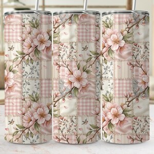 Puede incluir: Tres vasos de acero inoxidable con un diseño floral. El diseño presenta flores de cerezo rosas, hojas verdes y pequeños pájaros sobre un fondo de patchwork de cuadrados rosas, blancos y beige. Cada vaso tiene una tapa plateada y una pajita.