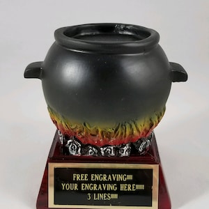 May include: Black cauldron trophy with a red and yellow flame base. The base has a gold plaque with the text "FREE ENGRAVING!!! YOUR ENGRAVING HERE!!! 3 LINES!!!"