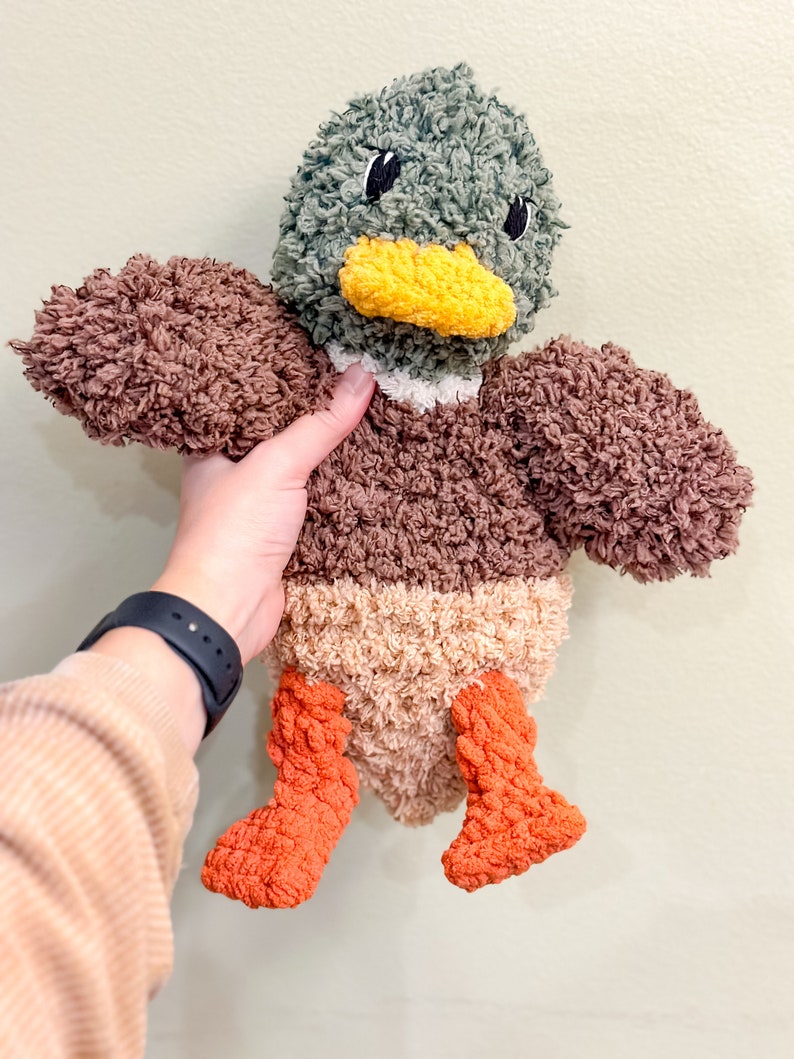 Op de afbeelding: Een pluche eendje met bruin, beige en oranje bont. De eend heeft een groene kop met zwarte ogen en een gele snavel.