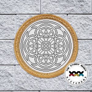May include: A black and white geometric design cross stitch pattern in a gold frame. The design is a circle with a repeating pattern of interlocking shapes. The frame is ornate and has a raised edge. The image is from The Sturdy Nerdy Stitchery.