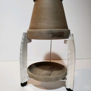 May include: A terracotta pot with a metal stand. The stand has two vertical supports and a round base. The pot is sitting on the stand.