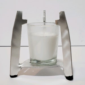 May include: A silver metal candle holder with a glass candle jar. The candle holder has a triangular base and two vertical supports.