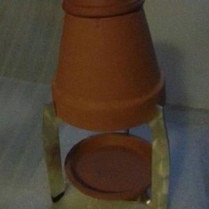 May include: A terracotta pot with a metal stand. The pot has a smooth, rounded shape and a slightly flared rim. The stand has three legs and is made of silver-colored metal.