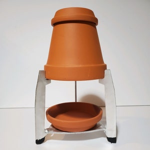 May include: A terracotta pot sits on a metal stand with a smaller terracotta dish underneath. The stand has two vertical supports and a horizontal bar connecting them.