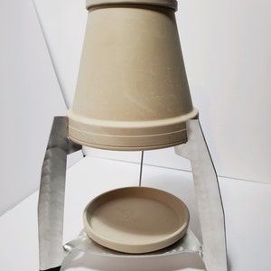 May include: A terracotta pot with a metal stand. The pot is on top of the stand and there is a smaller terracotta plate underneath the pot.