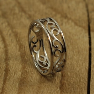 May include: A silver ring featuring a delicate, intricate design of swirling lines. The ring is made of metal and has a polished finish.