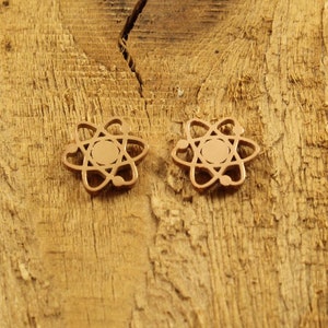 Może przedstawiać: Dwa złote kolczyki w kształcie atomu na drewnianej powierzchni.