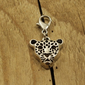 May include: Silver charm featuring a detailed leopard head design. The charm has a lobster clasp for attaching to a bracelet or necklace.