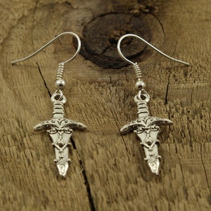 May include: A pair of silver dangle earrings featuring a sword design. The swords have intricate details and are suspended from silver hooks.