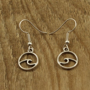 May include: A pair of silver earrings with a wave design. The earrings are hanging from a wooden surface.
