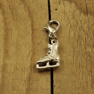 Op de afbeelding: Zilveren bedel in de vorm van een schaats. De bedel heeft een lus aan de bovenkant om aan een armband of ketting te bevestigen.