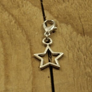 May include: Silver star-shaped charm with a clip on the top. The charm is on a wooden surface.
