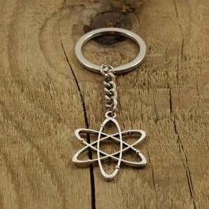 May include: Silver atom keychain with a silver ring and chain. The keychain is on a wooden surface.