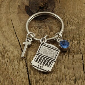 Może przedstawiać: Srebrny brelok do kluczy z zawieszką w kształcie laptopa, zawieszką w kształcie krzyża i zawieszką z niebieskiego kryształu.