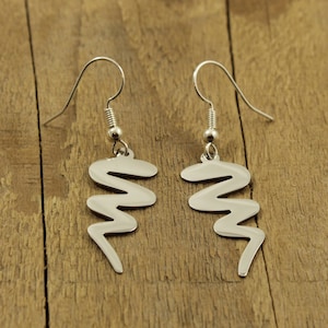 May include: A pair of silver earrings with a wavy, abstract design. The earrings are hanging from silver hooks.