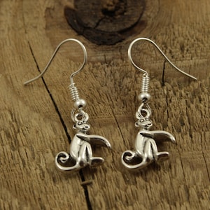 Puede incluir: Un par de pendientes de plata con forma de mono. Los monos están sentados con sus colas enroscadas alrededor de sus piernas.