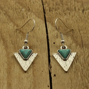 May include: A pair of silver triangle earrings with turquoise stones. The earrings have a hammered texture and a simple design.