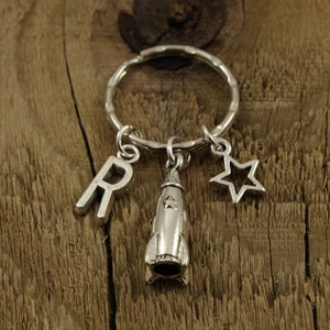 May include: Silver keyring with a rocket ship charm, a star charm, and a letter "R" charm. The charms are attached to a silver key ring.