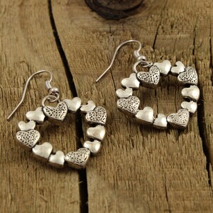 May include: A pair of silver heart-shaped earrings with a delicate design. Each earring is made up of a circle of small hearts.