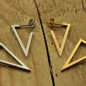 May include: A pair of triangle shaped earrings, one silver and one gold. The earrings are simple and modern in design.