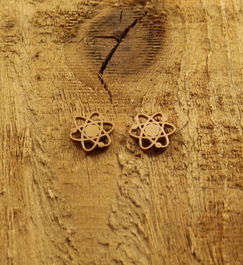 May include: Two gold-colored atom earrings on a wooden surface.