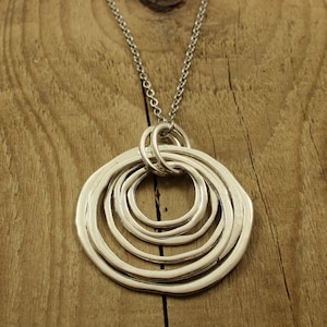 May include: A silver necklace with a pendant made of five interlocking circles. The circles are all different sizes and are arranged in a spiral pattern.