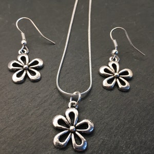 Pu&ograve; includere: Un set di collana e orecchini in argento con un delicato ciondolo a forma di fiore e orecchini abbinati. La collana ha una catena in argento e il ciondolo a forma di fiore &egrave; un design semplice e aperto.
