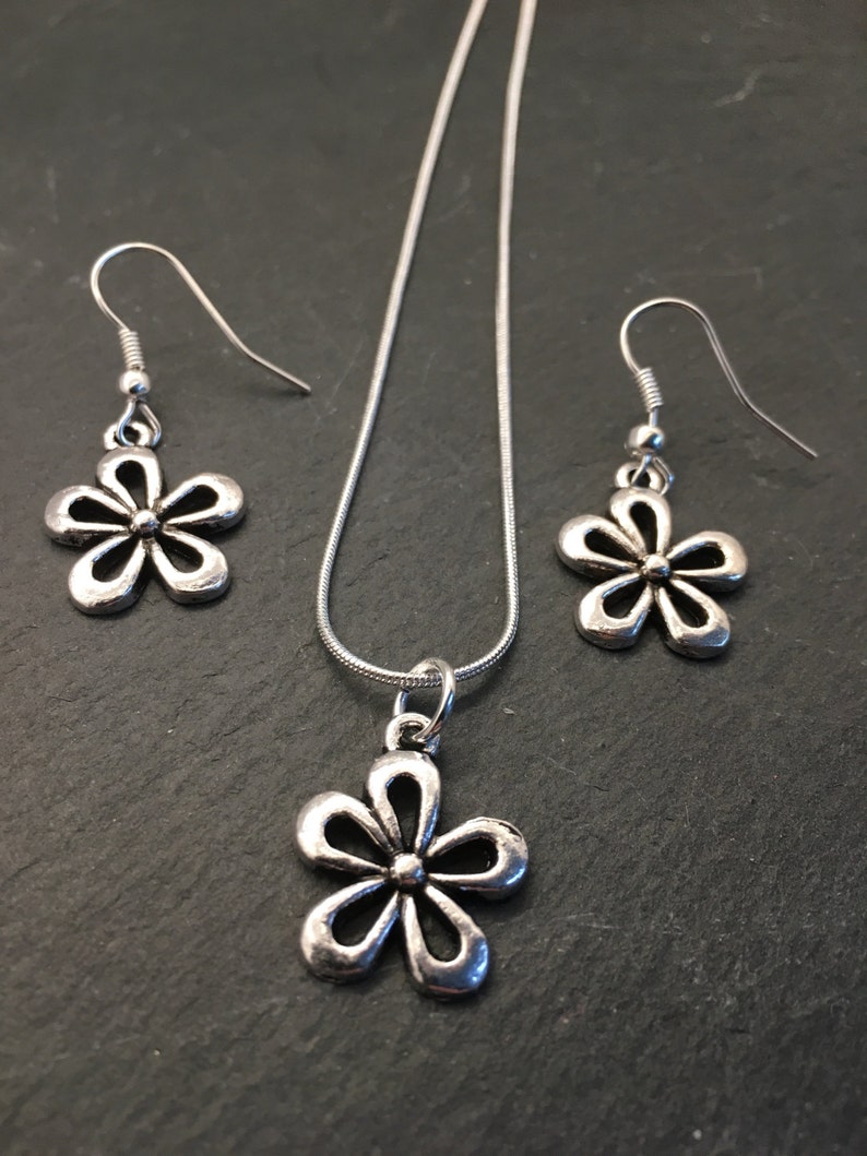 Pu&ograve; includere: Un set di collana e orecchini in argento con un delicato ciondolo a forma di fiore e orecchini abbinati. La collana ha una catena in argento e il ciondolo a forma di fiore &egrave; un design semplice e aperto.
